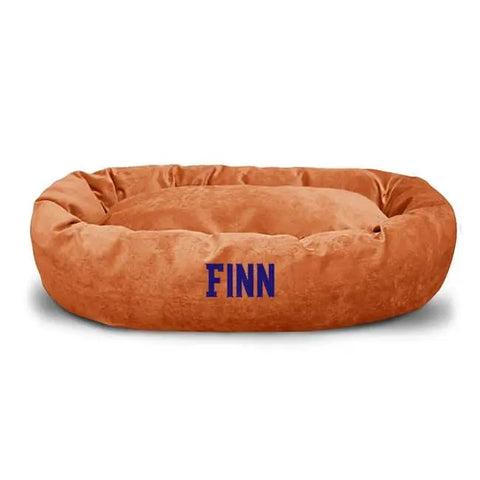 The Majestic Pet Villa Bagel Dog Bed - Personalized is oval, orange, and made of cozy micro-velvet, featuring FINN embroidered in blue on the front.