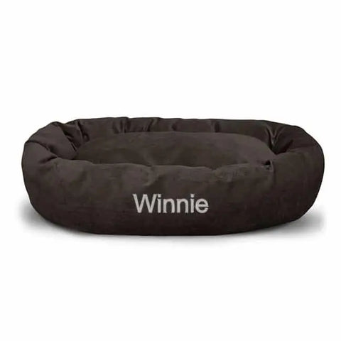 The Majestic Pet Villa Bagel Dog Bed - Personalized is a round, dark brown micro-velvet bed with a soft center and raised edges. Winnie is embroidered in white on the front, adding comfort and uniqueness for your pet.