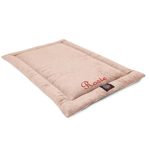 The Majestic Pet Villa Crate Mat - Personalized is a soft, rectangular beige dog mat with raised edges. Rosie is embroidered in red on one corner, and a logo tag accents the edge. This washable mat is perfect for easy cleaning.
