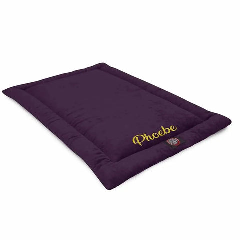 The Majestic Pet Villa Crate Mat - Personalized is a rectangular, dark purple dog bed with Phoebe embroidered in yellow and a logo patch at the corner. It has soft cushioned edges, a flat surface, and is machine washable.