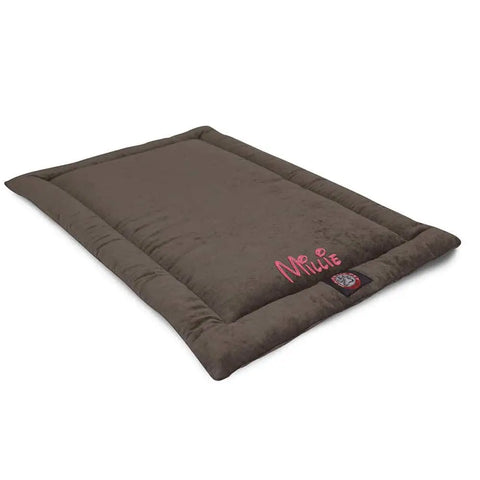The Villa Crate Mat - Personalized by Majestic Pet is a rectangular brown polyester dog bed with plush edges, featuring the name Millie embroidered in pink on one corner and a small logo tag near the edge.