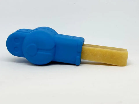 A yellow popsicle is partly held in a blue SodaPup Petz Yak Chew Holder EDispenser shaped like a cartoon character, lying on its side against a plain white background.