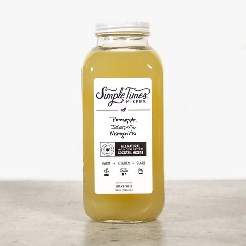 A clear Simple Times Mixers Pineapple Jalapeno Margarita bottle rests on a gray surface, showing its light yellow mixer—an all-natural, handcrafted blend ideal for distinctive margaritas.
