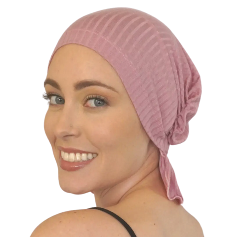 A smiling woman with light skin and blue eyes looks over her shoulder wearing the light pink, ribbed TAYLOR CHEMOBEANIE® by Chemo Beanies®—comfortable, stylish headwear for hair loss.