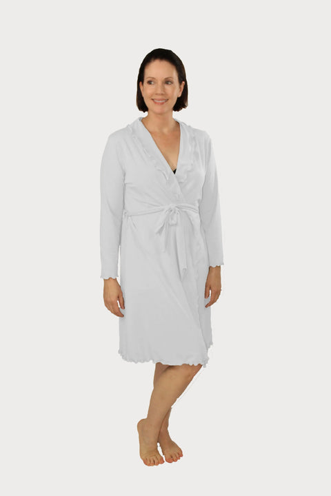 A woman with short brown hair smiles and looks to the side, standing barefoot in a Goodnighties Lettuce-Edge Robe with scalloped edges and a tie waist over a dark top, set against a plain white background.