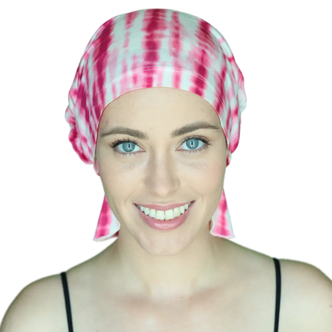 A smiling woman with bright blue eyes wears the Chemo Beanies® Tanisha headscarf and a black strap top, facing the camera against a plain background.