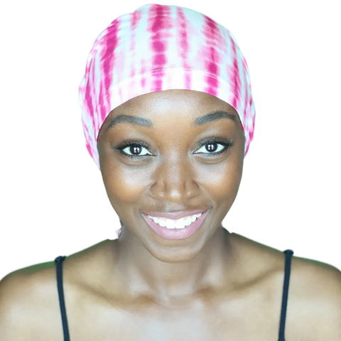 A smiling woman wears the Chemo Beanies® Scarves - Chemo Beanies® - Tanisha, a pink and white tie-dye slip-on beanie for hair loss, paired with a black spaghetti strap top, facing forward against a plain background.