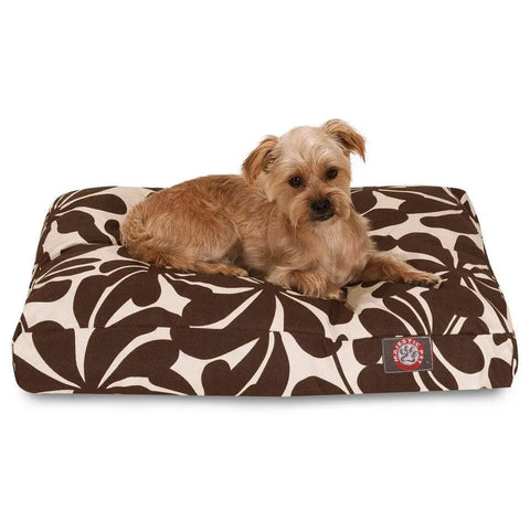A small, light brown dog relaxes on the Majestic Pet Plantation Rectangle Dog Bed, featuring a brown and white leaf pattern and premium polyester fill, shown against a plain white background.
