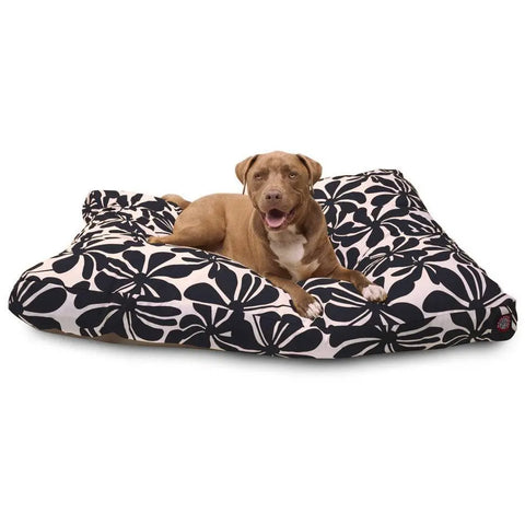 A brown dog with a white chest lies on a Majestic Pet Plantation Rectangle Dog Bed, featuring a black and white floral pattern, looking at the camera with its mouth open and tongue slightly out.