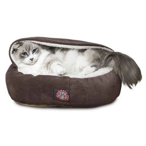 A fluffy gray and white cat lounges in the Majestic Pet Suede Canopy Cat Bed, a brown faux suede bed with a soft white lining. The red and white paw logo is visible as the relaxed cat’s tail sticks out of the partially covered design.