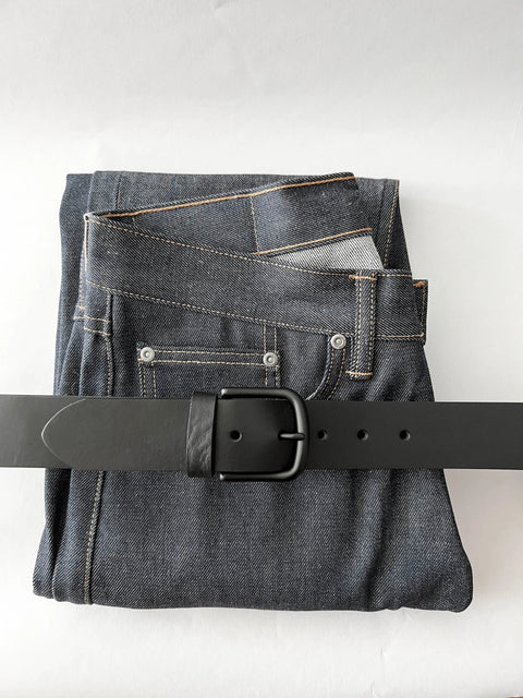 A pair of folded dark blue jeans with visible stitching rests on a white surface, topped with the Rogue Industries Baxter Leather Belt - 1.5 Wide, handcrafted from premium cowhide.