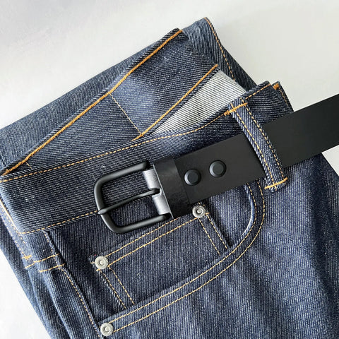 A pair of blue jeans with yellow stitching features the Rogue Industries Baxter Leather Belt (1.5 wide) threaded through the loops, all displayed on a white surface.