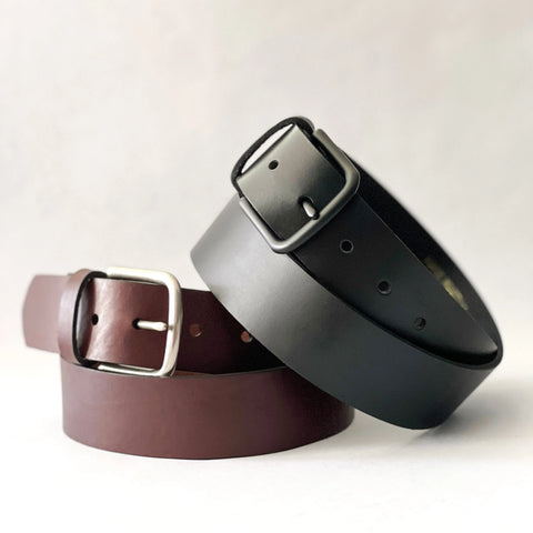Two Rogue Industries Baxter Leather Belts (1.5 wide)—one black with a black buckle, one dark brown with a silver buckle—overlapping on a plain background. Both are handcrafted and assembled in the USA.