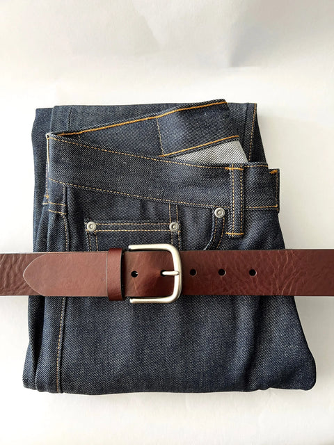 A pair of dark blue jeans neatly folded with the Rogue Industries Baxter Leather Belt - 1.5 Wide, made from premium cowhide leather, threaded through the belt loops and displayed on a white background.