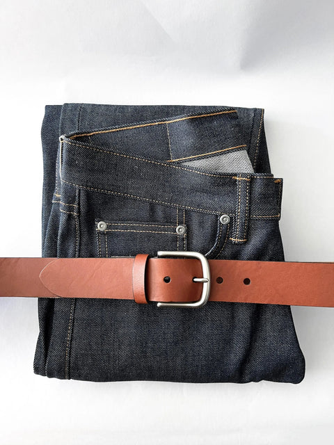 A pair of folded dark blue jeans with visible stitching, topped with Rogue Industries handcrafted Baxter Leather Belt—1.5 wide and made from premium cowhide leather with a silver buckle—all on a white surface.