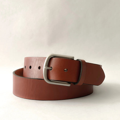 The Baxter Leather Belt by Rogue Industries, handcrafted from premium brown cowhide leather with a silver buckle, is coiled on a plain white background.