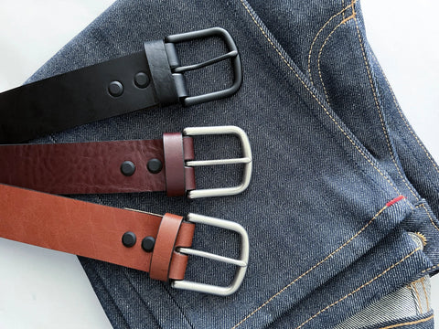Three Baxter Leather Belts by Rogue Industries—black, dark brown, and light brown—are displayed on blue denim. Each 1.5 wide belt is handcrafted from premium cowhide leather with silver or black buckles and double stud details.