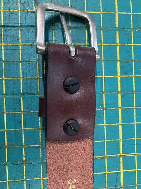 The Baxter Leather Belt - 1.5 Wide by Rogue Industries features premium cowhide leather, a silver buckle, and two black Chicago screws. Assembled in the USA, its shown on a green grid-patterned cutting mat.