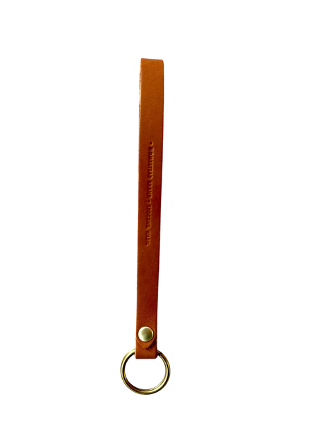 The Homestead Brand Standard Wristlet No. 1604 is a handmade brown full grain leather keychain strap with a gold metal ring and metal rivet, crafted in the USA and shown against a black background.