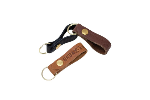 Three Urban Southern Urban Key Fob leather keychains—black, dark brown, and tan—each with a brass button and keyring. The tan and dark brown key fobs are embossed with URBAN Soul. Photographed on a white background.