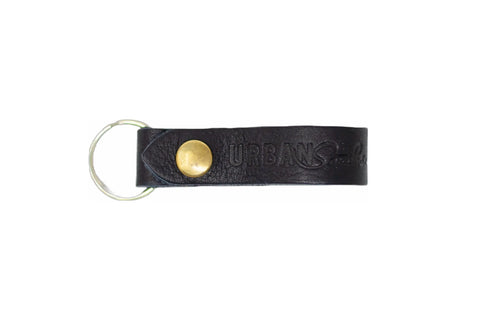 The Urban Southern Urban Key Fob is made of black genuine leather with a brass snap button, metal keyring, and URBANS embossed on the strap.