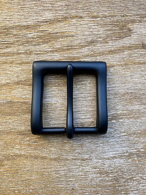 A BBH Handcrafted Leather Belt’s black metal square buckle rests on a textured wooden surface, showcasing artisan quality.