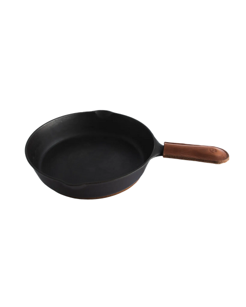 A black cast iron skillet with the Homestead Brand Skillet Handle Sleeve No. 2002 made of full grain leather rests on a white background.