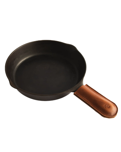 The Homestead Brand Skillet Handle Sleeve No. 2002, a brown leather cover, adds style and protection to the black cast iron skillet displayed on a white background.