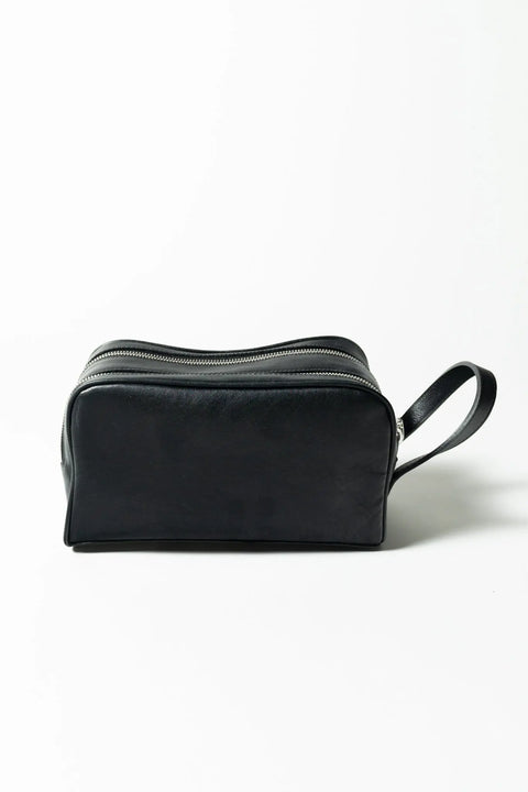 The Midnight Dopp Kit by Marc Nelson is a black handmade leather bag with two zippered compartments and a side handle, perfect for stylish travelers. Shown on a white background.
