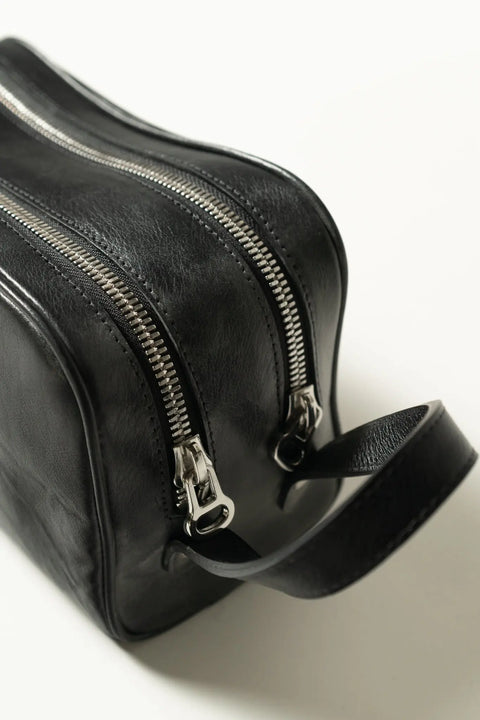 The Midnight Dopp Kit by Marc Nelson is a black handmade leather dopp kit with two silver zippers and a sturdy handle, shown on a white background—ideal for stylish travelers.