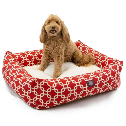 A small, curly-haired brown dog sits happily in the stylish, machine-washable Majestic Pet Links Luxe Bagel Bed, featuring a plush white cushion and a luxurious red and white pattern.