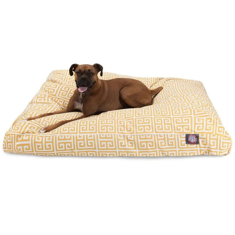 A brown dog lies on the Majestic Pet Towers Rectangle Dog Bed, featuring a yellow and white pattern and a removable cover, looking at the camera with its mouth open and tongue out.