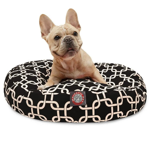 A light brown French Bulldog sits upright on a washable Majestic Pet Links Round Dog Bed with a removable cover, white interlocking pattern, and red and white Pawstic label.
