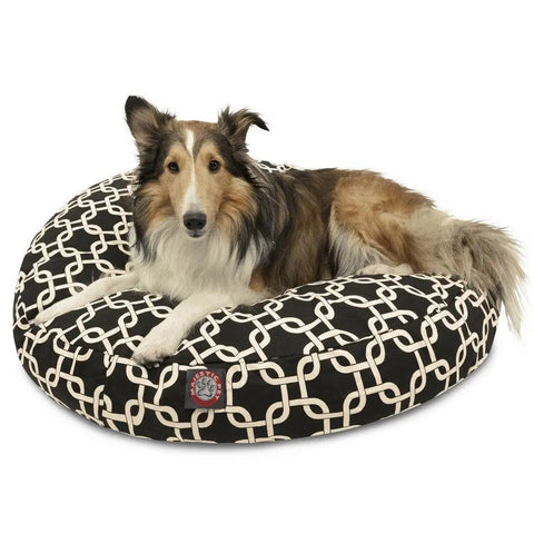 A long-haired dog with a brown, black, and white coat lies on the Majestic Pet Links Round Dog Bed, featuring an interlocking white pattern and a washable, removable cover to keep it fresh. The alert pup looks toward the camera.