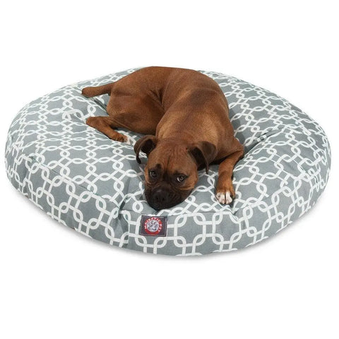 A brown dog with a black snout lies on the Majestic Pet Links Round Dog Bed, which features a gray and white pattern and a removable cover, looking up with a relaxed expression.