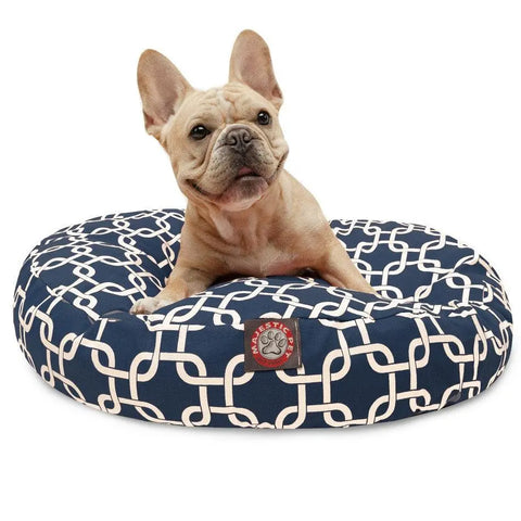A light brown French Bulldog sits on the Majestic Pet Links Round Dog Bed, a navy blue bed with a white geometric pattern, removable cover, and red logo patch.