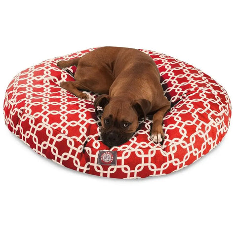 A brown dog lies on the Majestic Pet Links Round Dog Bed, featuring a large red design with a white interlocking chain pattern and a removable cover.