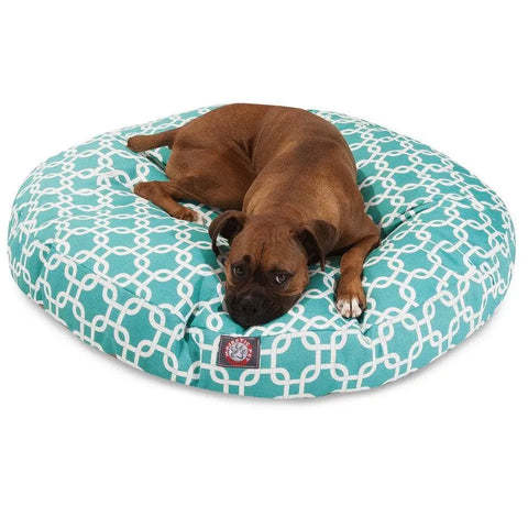 A brown dog relaxes on the Majestic Pet Links Round Dog Bed, featuring a washable, removable cover in teal with a white geometric pattern. The dog lies comfortably with its head and legs stretched out.