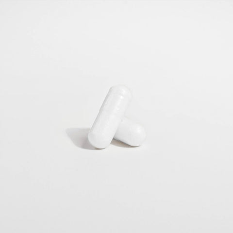 Two white capsules of Norri Nutrition Probiotic 40 Billion CFUs With Prebiotics are arranged on a plain white background, with one capsule resting against and partially overlapping the other in this minimalistic, well-lit scene.