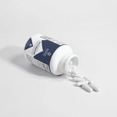 A white bottle of Norri Nutrition Probiotic 40 Billion CFUs With Prebiotics lies on its side, with several white capsules spilling onto a white surface.
