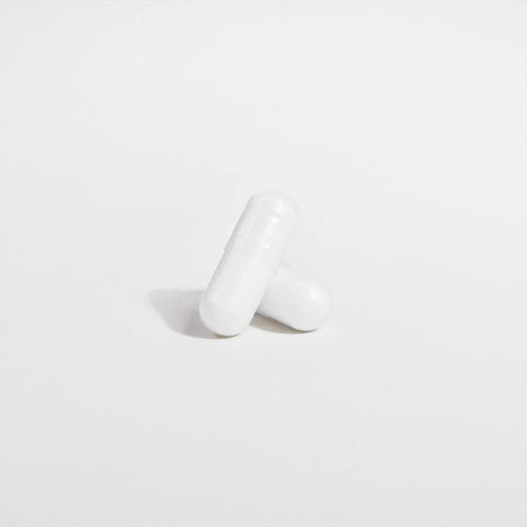 Two white capsules rest on a plain surface, highlighting Norri Nutrition’s Probiotic 40 Billion CFUs With Prebiotics—a supplement crafted to support digestive health.