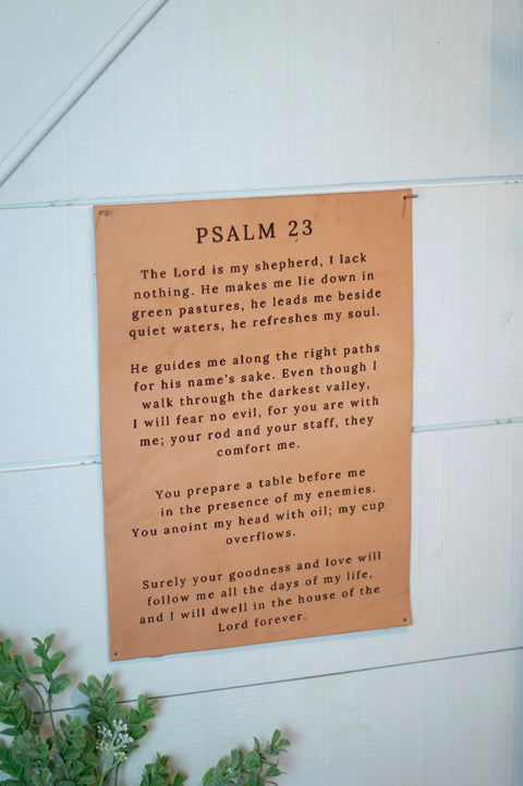 The Urban Southern Psalm 23 Leather Sign features black script on tan leather, displaying the comforting Bible passage. Handcrafted and stylish, it adds inspiration when hung on a light wooden wall beside greenery.