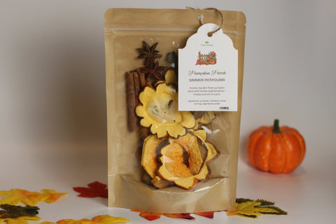 A brown resealable bag of Forev'Herbs Pumpkin Patch Simmer Potpourri with dried fruit and spices, labeled with a white tag, sits on a white surface surrounded by a small pumpkin and artificial leaves—a cozy autumn home fragrance.