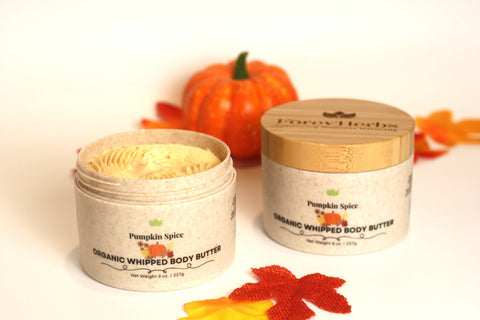 Two jars of Forev'Herbs Pumpkin Spice Organic Whipped Body Butter, one open to show its creamy texture, sit beside a pumpkin and autumn leaves—ideal for deep hydration and cozy seasonal vibes this fall.