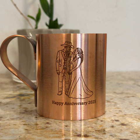The Havens Luxury Metals Pure Copper Mule Mug, engraved with a wedding couple and Happy Anniversary 2025, showcases American craftsmanship as it sits on a granite countertop, with a potted plant in the background.