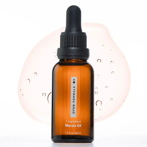 A brown glass dropper bottle labeled Open Formula Marula Oil is pictured before a light pink liquid drop. This 1 fl oz (30 ml) marula oil moisturizes and protects hair.