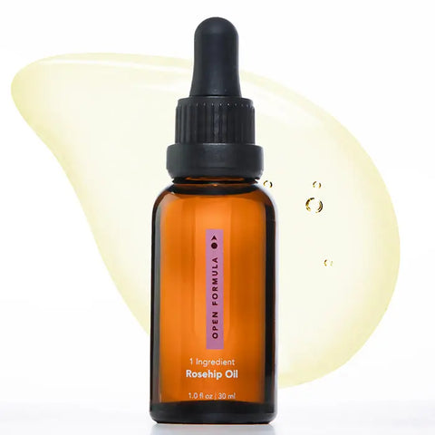 An amber dropper bottle labeled Open Formula Rosehip Oil stands before a light yellow oil smear with air bubbles on a white background—ideal for natural skincare routines seeking pure rosehip oil benefits.