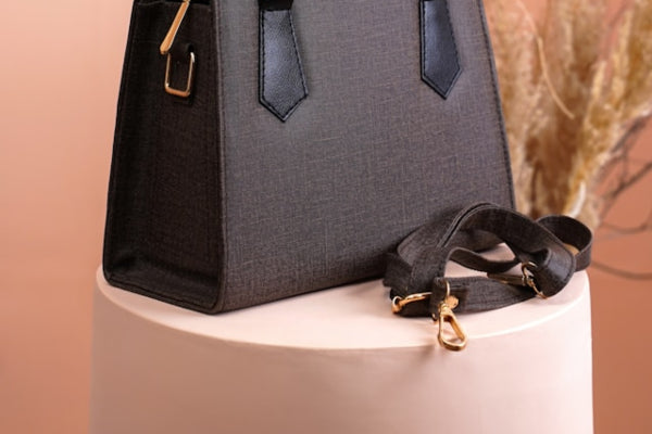 Gray handbag with a strap on a white pedestal against a beige background