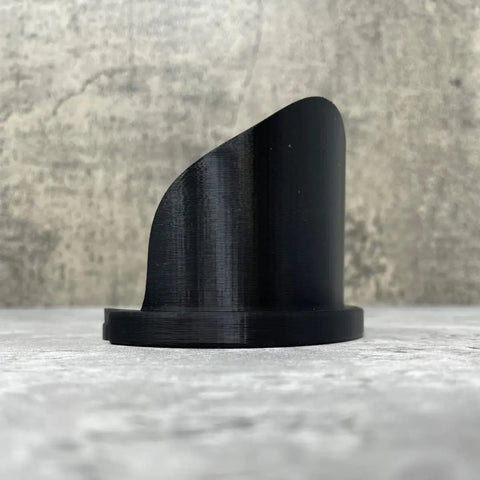 The Chatelet Manufacturing Paint Can Pourer, made in the USA, is a black, glossy 3D-printed tool with a curved asymmetrical top that fits quart-sized paint cans for no-mess pouring—shown on a textured gray surface against a concrete-style background.