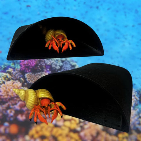 Two orange hermit crabs with yellow shells rest inside Chatelet Manufacturing’s REEFSHAPE Aquarium Pocket Cave, a minimalist black shelter by coral on a blue underwater backdrop. Made in the USA for fish, shrimp, reptiles & more.